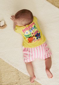 T-shirt jaune avec des graphismes floraux colorés et le texte "HAPPY and bright", associé à un short rayé rose et blanc sur une surface texturée.