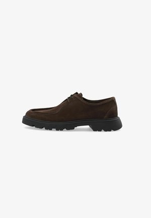 Chaussure en suede marron au design arrondi, dotée d'une semelle en caoutchouc noir et d'un système de laçage. Texture lisse avec des accents minimaux.