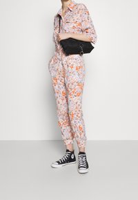 Monos de flores en colores pastel con acentos naranjas, bolsillos grandes y tobillos remangados, combinados con zapatillas negras de caña alta.