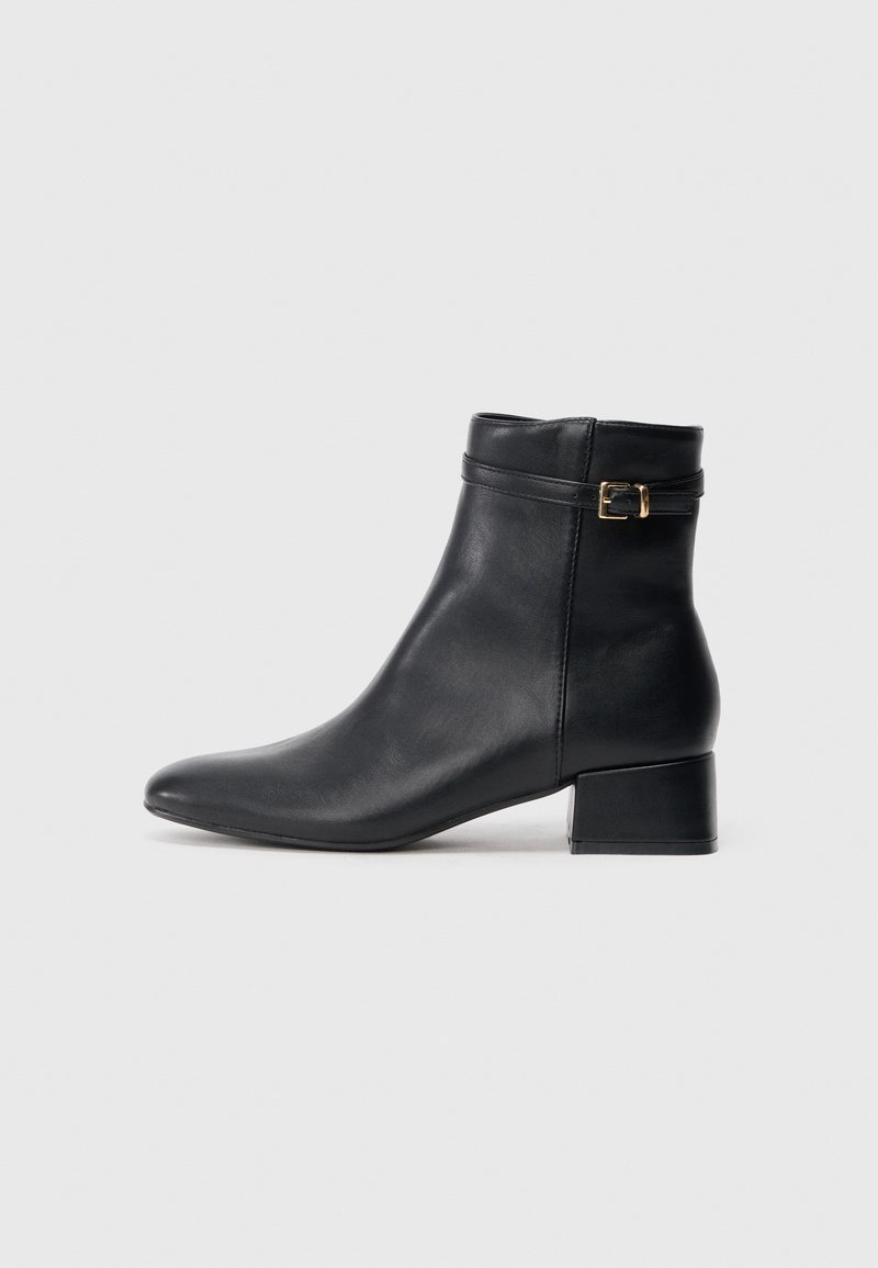 Bota preta de couro até ao tornozelo com bico arredondado, salto baixo e bloco, e uma tira decorativa com um detalhe em fivela dourada. Textura suave, design minimalista.