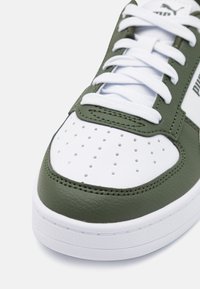 Baskets vertes et blanches en cuir texturé avec une boîte à orteils perforée, des lacets blancs plats et des accents cousus le long des bords.