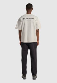 Koszulka off-duty w kolorze kremowym z krótkimi rękawami. Z tyłu widnieje wyraźny czarny napis. Połączona z ciemnymi spodniami i szarymi sneakersami.