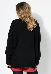 Czarny oversize sweter o prążkowanej teksturze, z opadającymi ramionami i szerokimi rękawami, w połączeniu z czerwonymi szortami. Prosty i luźny krój.