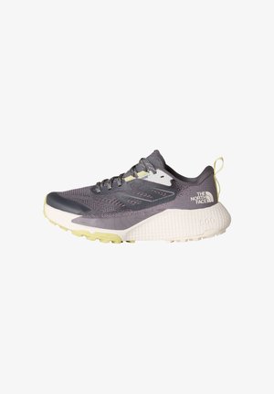 Zapatilla deportiva gris con parte superior texturizada, puntera reforzada y media suela blanca. Presenta una suela con patrón y acentos amarillos.