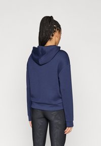 Sweatshirt com capuz azul marinho em tecido suave, com um corte descontraído, apresentando um bolso canguru e punhos canelados, combinado com leggings pretas estampadas.