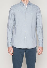 Ljusblå, knäppskjorta i ett mjukt, texturerat tyg. Har klassisk krage, långa ärmar och en slim fit-design med diskret varumärkeslogotyp.