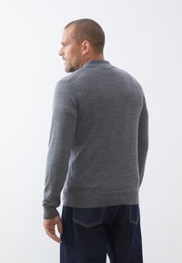 Grå langærmet sweater med en tætsiddende krave, glat tekstur og ribbede manchetter, parret med mørkeblå jeans. Minimalistisk design, ingen mønstre.
