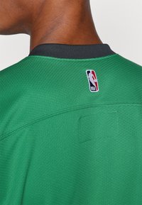 Zöld NBA mez fekete gallérral, oldalvarrással és logóapplikációval. Az anyag texturált felületű.