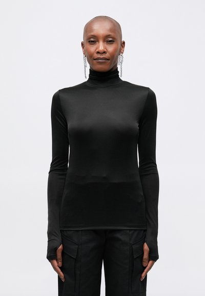 Maglia nera a maniche lunghe con collo alto, realizzata in tessuto liscio e elasticizzato, con maniche aderenti dotate di aperture per il pollice. Indossata con pantaloni cargo neri.