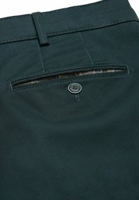 Donkergroene broek gemaakt van gestructureerde stof, met een achterzak met knoopsluiting en een zichtbare gevoerde binnenkant met patroon.