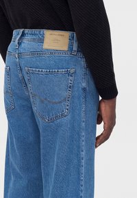 Άτομο που φοράει ανοιχτό μπλε τζιν Jack & Jones με μαύρο τοπ μακρυμάνικο, εμφανίζοντας τις πίσω τσέπες και την ετικέτα της μάρκας στη μέση.