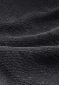 Close-up of textured black fabric with visible diagonal weave and soft folds creating gentle shadows and highlights.