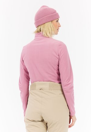 Maglietta a maniche lunghe in fleece di un rosa soft, con collo alto e texture a costine. Abbinata a pantaloni beige con vita elastica.