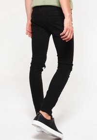 Jeans ajustados negros con un diseño clásico, textura suave, estilo con cinco bolsillos y detalles de costuras sutiles, combinados con zapatos negros sin cordones.