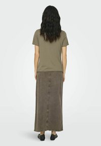 T-shirt en coton vert olive associé à une longue jupe en denim marron. La jupe présente une couture centrale et un ourlet effiloché. Chaussures noires à enfiler.
