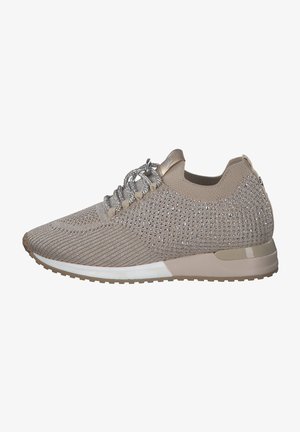 Zapatilla deportiva beige con parte superior de punto texturizado, acentuada con adornos plateados y cordones reflectantes; suela ligera con un borde blanco.