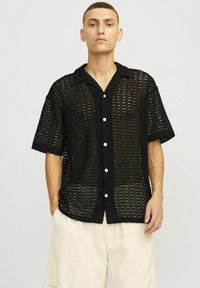 Czarna koronkowa koszula z krótkimi rękawami, o otwartym wzorze, z białymi guzikami. Posiada kołnierzyk i luźny krój.