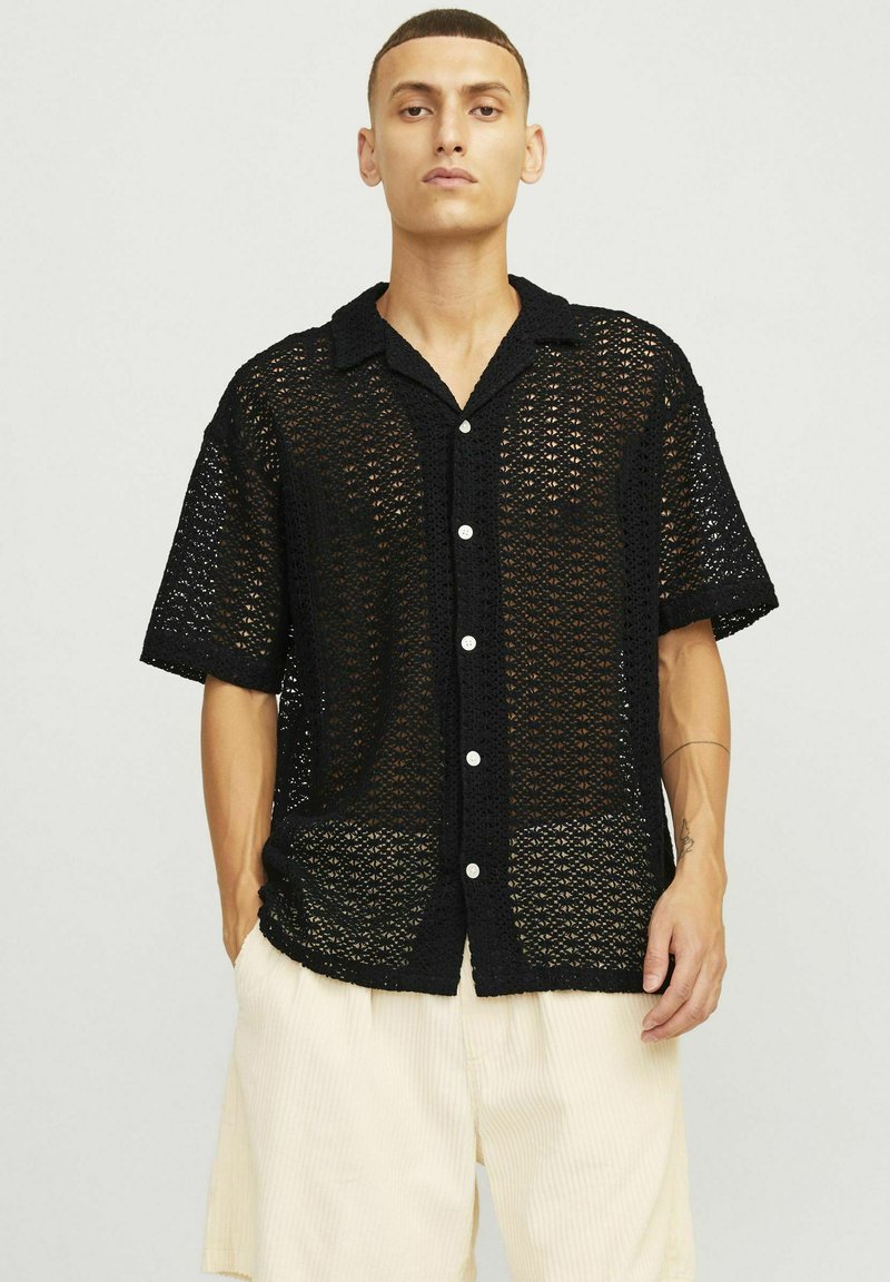 Czarna koronkowa koszula z krótkimi rękawami, o otwartym wzorze, z białymi guzikami. Posiada kołnierzyk i luźny krój.