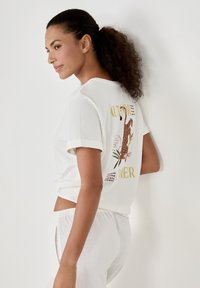 Weißes Kurzarm-T-Shirt mit Rundhalsausschnitt, das auf der Rückseite ein buntes grafisches Design mit Blatt- und Tiermotiven in verschiedenen Farben zeigt.