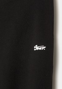 Črn bombažni material z belim logotipom, ki prebere "Stwz." Tekstura je videti gladka z rahlo elastičnim zaključkom.