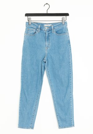 Jasnoniebieskie, dżinsowe spodnie z wysokim stanem, przednimi kieszeniami i zapięciem na guziki, wiszące na czarnym wieszaku na białym tle.