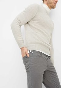 Lichtgrijze gebreide trui met geribbelde textuur; nauwsluitende stijl. Gecombineerd met grijze corduroy broek met voorzakken en knoopaccenten.