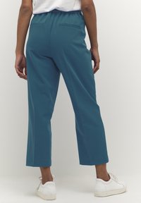 Teal cropped pants met een elastische tailleband, twee achterzakken en een gladde textuur, gecombineerd met witte sneakers.