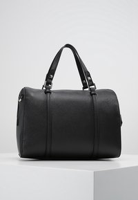 Svart duffelväska gjord av texturerat syntetiskt material, med två handtag upptill och detaljer i silver. Rundad form med sömdetaljer.