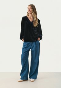 Zwarte fluwelen top met een V-hals en pofmouwen, gecombineerd met brede blauwe denim broek, gedragen met casual witte schoenen.