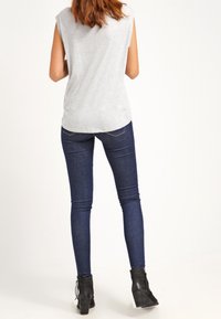 Gray sleeveless top paired with dark blue skinny jeans. The jeans feature a five-pocket design and are complemented by black ankle boots.