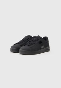 Une paire de baskets basses noires avec des lacets et des semelles épaisses, arborant des accents de marque subtils sur le côté et la languette.