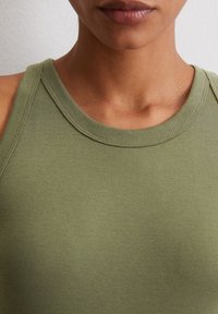 Débardeur vert olive avec une texture côtelée, se distinguant par un encolure ronde et de larges bretelles. Finitions avec des coutures sur les bords.