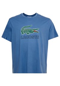 Niebieska bawełniana koszulka z zielonym nadrukiem krokodyla i napisem "LACOSTE" poniżej. Krótkie rękawy, okrągły dekolt, swobodny krój.