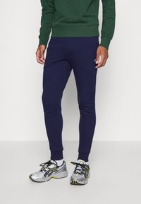 Pantalones jogger azul marino de corte ajustado, fabricados en un tejido suave con puños acanalados, combinados con zapatillas deportivas plateadas y negras con acentos amarillos.