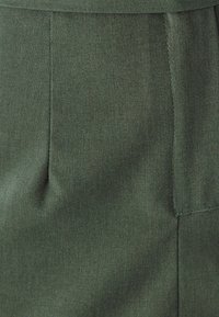 Tessuto verde scuro con una trama liscia, caratterizzato da una piega e dettagli di cucitura lungo i bordi. Il design presenta un taglio semplice ed elegante.