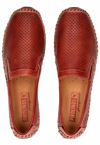Zapatos slip-on perforados rojos con parte superior de cuero suave, costuras en contraste y suela ligera. El interior presenta una marca en relieve.