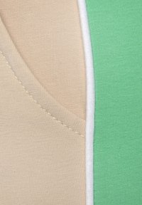 Textilstoff in Beige- und Grüntönen, mit glatter, dehnbarer Textur. Sichtbare Nähte entlang der Ränder, mit einem sauberen Schnitt am Rand.