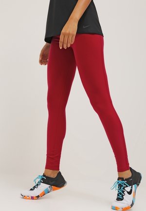 Leggings de sport rouges en tissu extensible, associés à des chaussures de sport multicolores noir et blanc avec des accents bleus.