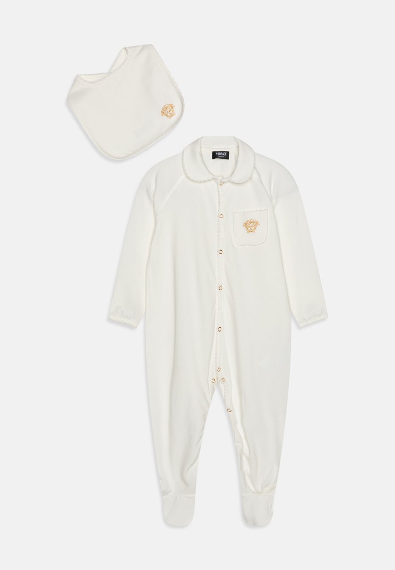 Pijama de felpa blanca para bebés con cuello, botones dorados y un bolsillo que presenta un logo dorado. Incluye un babero blanco a juego con detalles de costura.