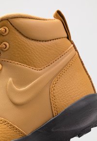 Wysokie tenisówki Nike w kolorze beżowym z teksturowaną cholewką ze skóry, gładkimi akcentami, wiązaniem na sznurowadła oraz czarną gumową podeszwą.