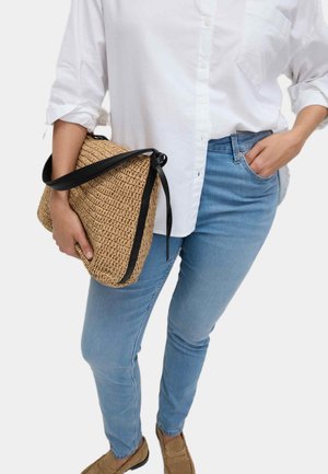 Vävd halmhandväska med ett svart band, hålls mot en vit skjorta och blå jeans. Har texturerat material och en avslappnad design.
