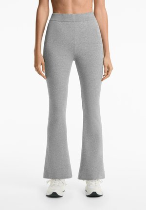 Grijze flare legging van rekbaar materiaal, met een hoge tailleband en een soepele textuur, gecombineerd met witte sportschoenen.