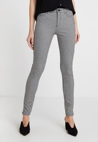 Černobílé kalhoty s kostkovaným vzorem ve slim fit provedení, vyrobené z pružného materiálu, s uzávěrem na zip a knoflík.