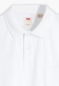 Hvit polo skjorte med myk tekstur, standard krage, tre knapper, og en subtil Levi's-logo preget på stoffet. Vintage passform.