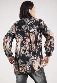 Woven schwarze Bluse mit beigem und braunem Blumenmuster, langen Ärmeln, elastischen Bündchen und einem abgerundeten Saum. Leichter Stoff mit einer glatten Textur.
