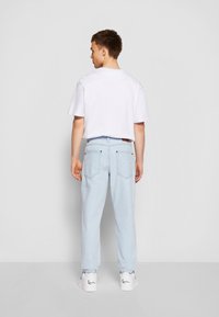 Jasnoniebieskie dżinsy z tapered fit, z dwiema tylnymi kieszeniami, w zestawieniu z białą koszulą z krótkim rękawem i białymi trampkami.