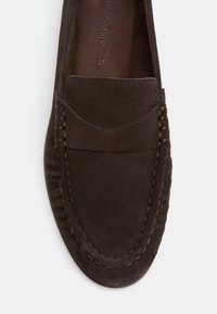 Mocassin en daim brun foncé avec coutures visibles le long des bords, bout arrondi et taille 37 indiquée à l’intérieur.
