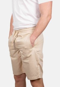 Pantaloni corti beige realizzati in tessuto leggero, con vita elastica e cordoncino, tasche laterali e una vestibilità comoda.