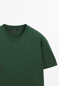 T-shirt vert foncé à col rond, manches courtes, col côtelé et petite étiquette noire à l'intérieur de l'encolure.