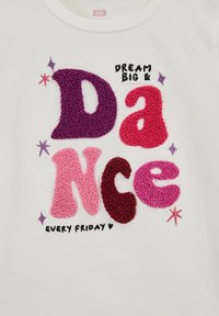 Fehér pulóver színes, texturált betűkkel, amelyek a "DREAM BIG & DANCE EVERY FRIDAY" feliratot formálják, csillagokkal és szív díszítéssel.